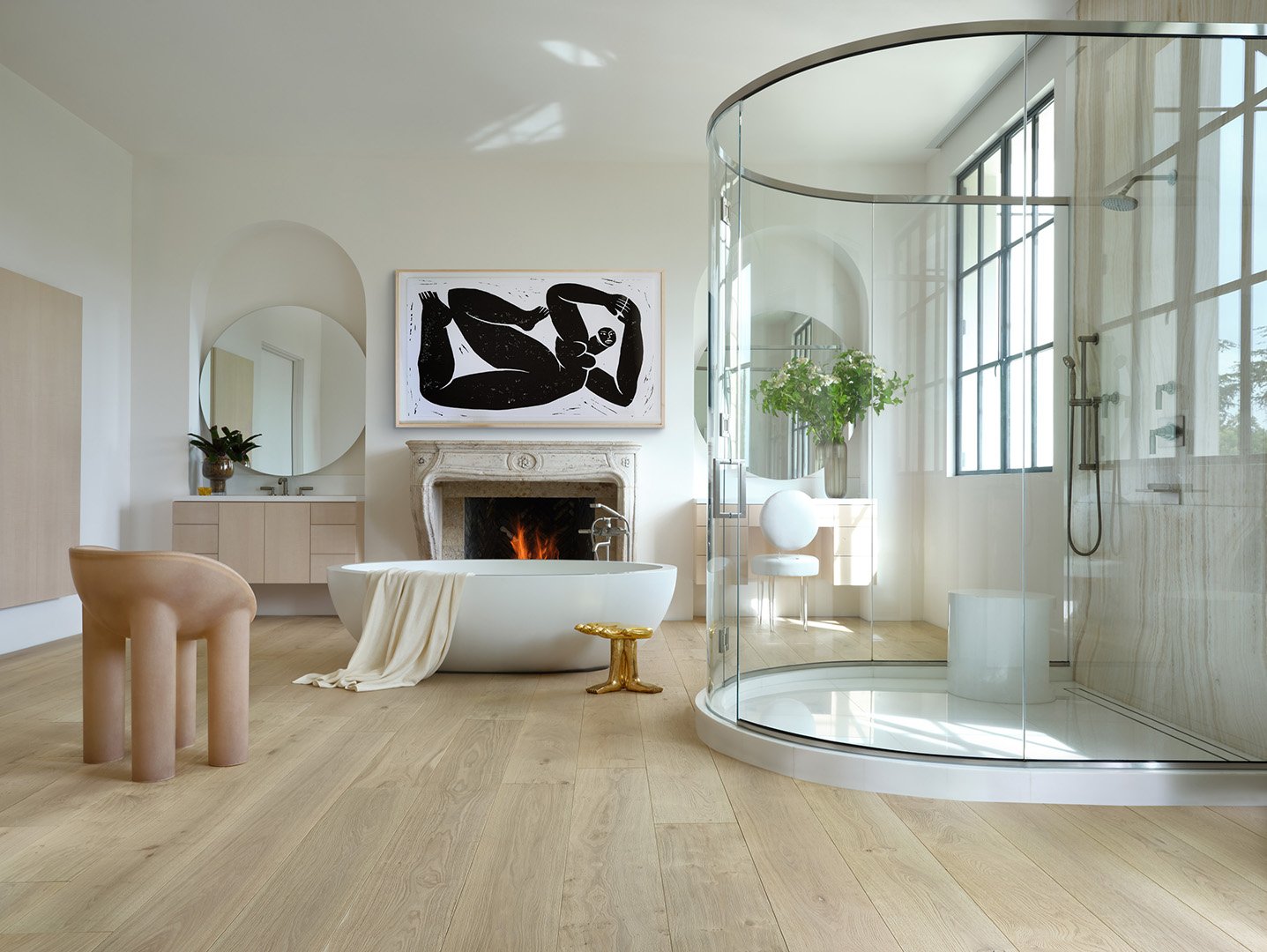 Interior styling of a luxury bathroom for California Classic Floors featuring a large half circle glass shower, an oval soaking tub, modern seating and accents, custom artwork and a fireplace, styled by Stephen Pappas Interiors, photographed by Roger
